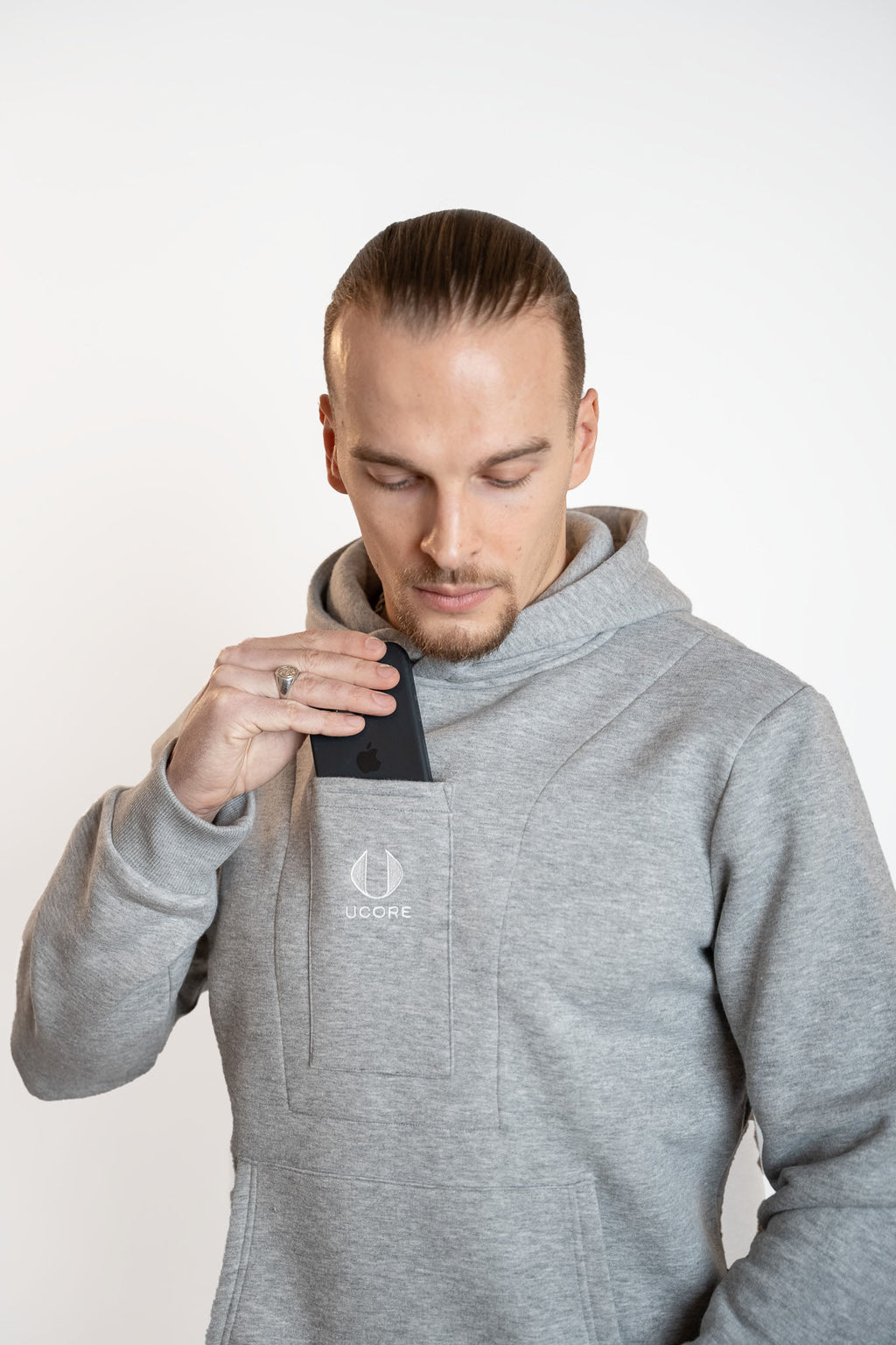 man putting phone into central pocket of men's grey ucore hoodie