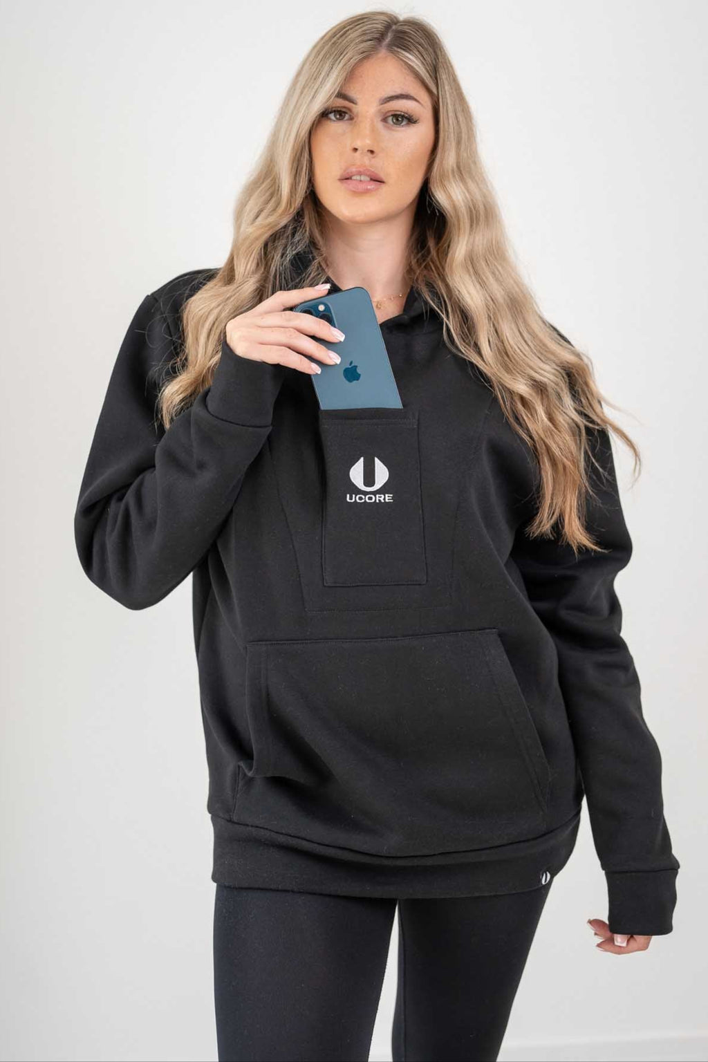 model placing phone in the central pocket of a ucore women's black hoodie 