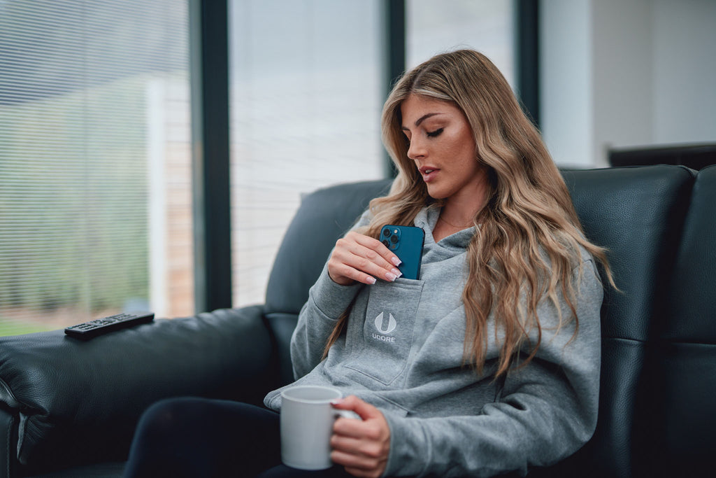 model sitting of sofa taking phone out of a grey ucore hoodie's central pocket