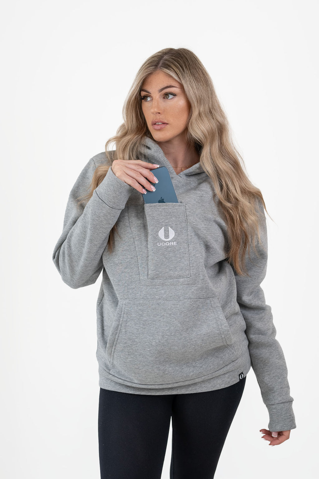 model wearing women's grey ucore hoodie putting phone in central pocket.